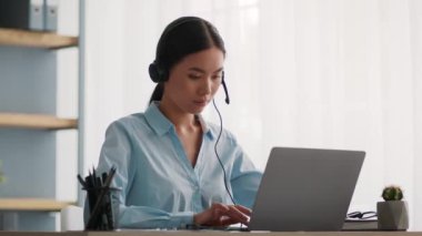 Koreli Ofis İşçisi Kadın Laptop kullanıyor. Kapalı alanda kulaklık takıyor.