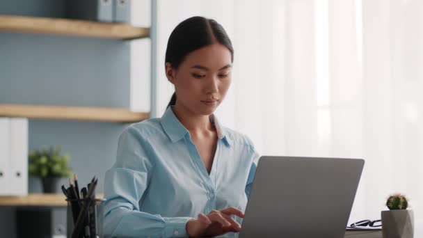 Mujer de negocios asiática seria usando computadora portátil escribiendo en la oficina — Vídeos de Stock