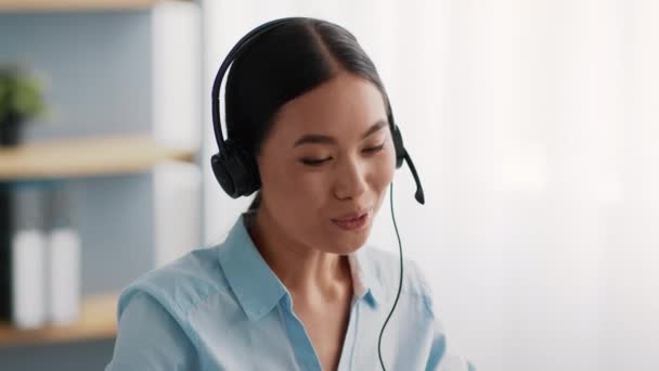 Alegre operador de línea de ayuda asiática hablando con auriculares en la oficina — Vídeo de stock