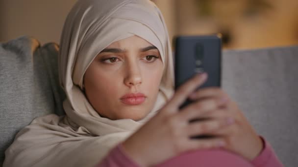 衝撃的な内容だ 若いですびっくりしたイスラム教徒女性のポルノのハイジャブビデオを見ます上のスマートフォンと感じ唖然と 上のソファに家で夜 遅い動き — ストック動画