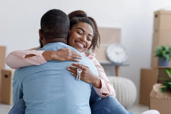 Sonriendo millennial africana americana esposa abrazando marido en nuevo apartamento, dama mantenga llaves en la habitación con cajas —  Fotos de Stock