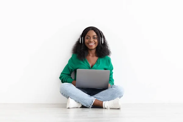 Mulher preta bonita com laptop e fone de ouvido sem fio no branco — Fotografia de Stock
