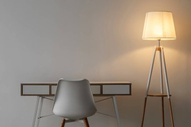 Beyaz boş sandalye, masa ve parıldayan lamba gri duvar arka planında ofis veya oturma odasında