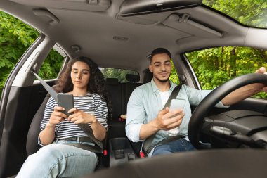 Arabayla seyahat ederken akıllı telefon kullanan Arap erkek ve kadın