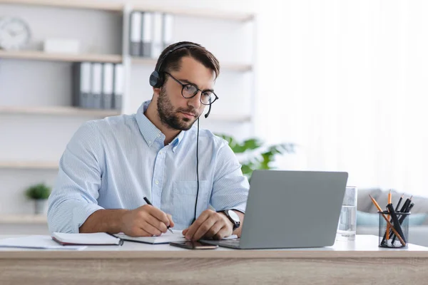 Drukke volwassen europese man manager met baard in bril en koptelefoon werken op laptop in kantoor — Stockfoto