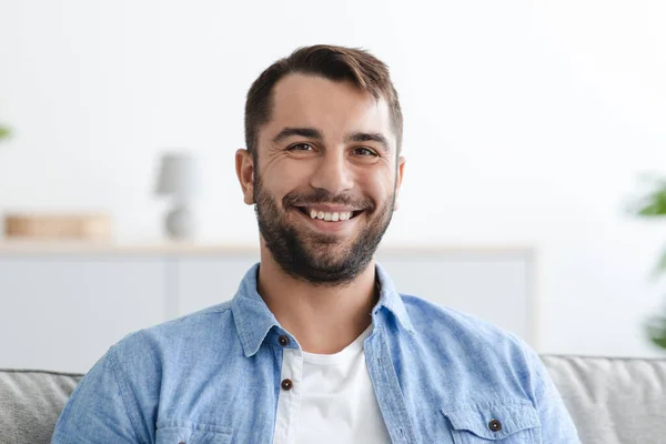 Huvudbild av glad vuxen europeisk man med skägg tittar på kameran i vardagsrummet interiör — Stockfoto