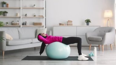 Sırt güçlendirme pratiği. Genç Arap kadın başörtüsü takıyor evde spor yaparken mekik çekiyor.