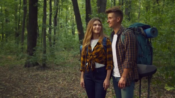 Активное разрешение на отдых. Молодая счастливая пара туристов, стоящих в лесу с рюкзаками и жестом вверх — стоковое видео
