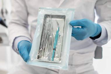 Mavi Steril Eldiven Giyen Doktor Diş Aracı ile Mühürlü Sterilizasyon Kesesini Gösteriyor