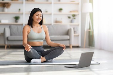 Çevrimiçi yoga. Genç Asyalı kadın evde meditasyon yapmak için dizüstü bilgisayar kullanıyor.