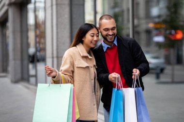 Sevecen, çok uluslu bir çift süpermarketin yanında duruyor, alışveriş torbalarının içine bakıyor, birlikte alışverişe çıkıyorlar.