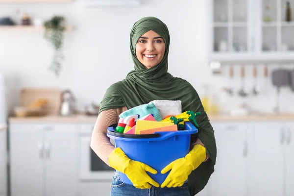 Alegre jovem dona de casa islâmica segurando balde com suprimentos de limpeza — Fotografia de Stock