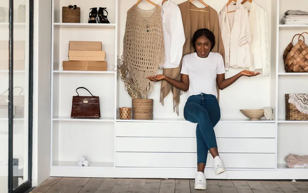 Mujer afroamericana confusa encogiéndose de hombros sentada en el vestuario —  Fotos de Stock