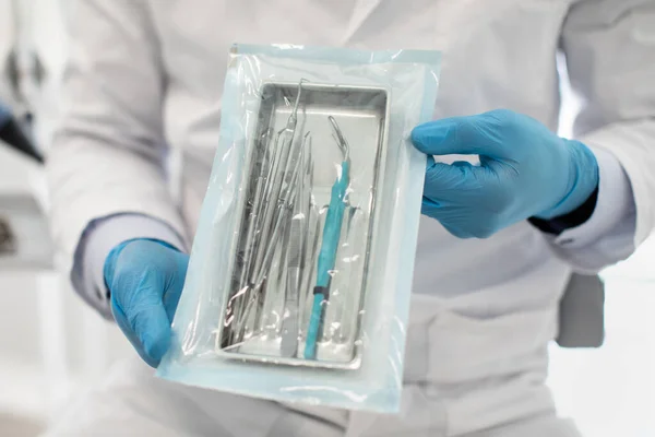 Doctor con guantes estériles azules Demostración de bolsa de esterilización sellada con herramientas dentales —  Fotos de Stock
