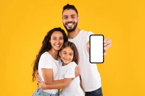 Família árabe feliz mostrando smartphone com tela em branco, fundo amarelo — Fotografia de Stock