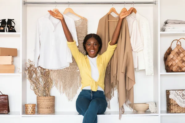 Mulher negra excitada sentada no guarda-roupa entre roupas novas interior — Fotografia de Stock