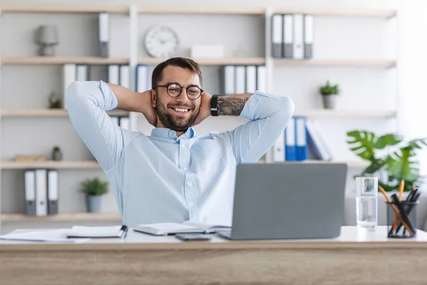 Heureux homme européen mature avec barbe dans des lunettes avec les mains derrière la tête reposant sur le travail à distance derrière un ordinateur portable — Photo