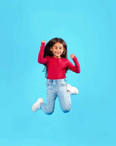 Niña saltando divirtiéndose posando en medio del aire, fondo azul — Foto de Stock