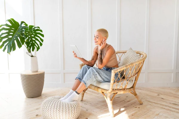 Νεαρή καυκάσια γυναίκα που χρησιμοποιεί ψηφιακή ταμπλέτα ενώ αναπαύεται σε ψάθινη καρέκλα πάνω από λευκό τοίχο, ελεύθερος χώρος — Φωτογραφία Αρχείου