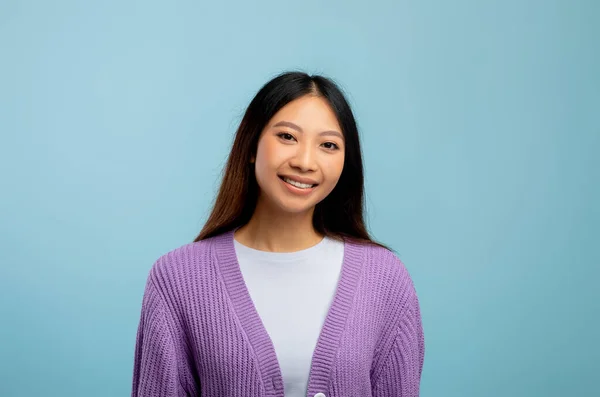 Porträt einer glücklichen asiatischen Dame mit langen dunklen Haaren, die vor blauem Hintergrund posiert und in die Kamera lächelt — Stockfoto