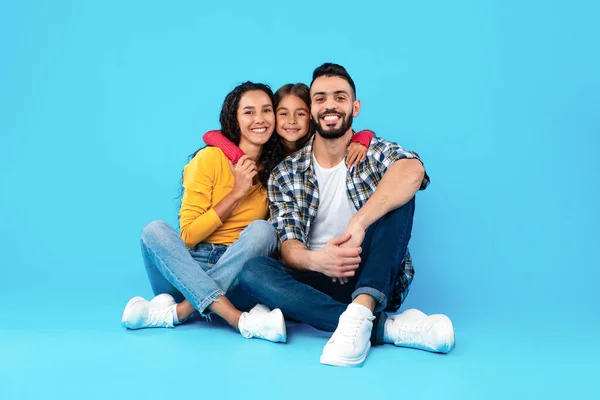 Aimer famille arabe étreignant assis dans le studio sur fond bleu — Photo