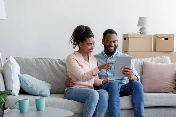 Tevreden jonge Afrikaanse Amerikaanse man en vrouw zitten op de bank met kartonnen dozen en het plannen van een nieuw ontwerp — Stockfoto