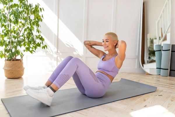 Tausendjährige Kaukasierin hält sich zu Hause fit. Sportliche Dame trainiert ihre Bauchmuskeln auf Yogamatte — Stockfoto