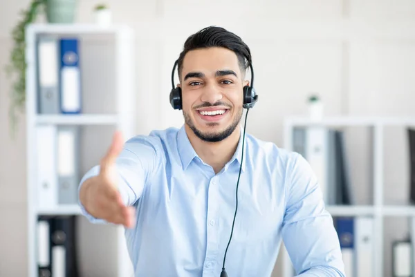 Homme arabe heureux dans les écouteurs ayant un appel vidéo en ligne avec un partenaire d'affaires, offrant poignée de main, faire affaire au bureau — Photo