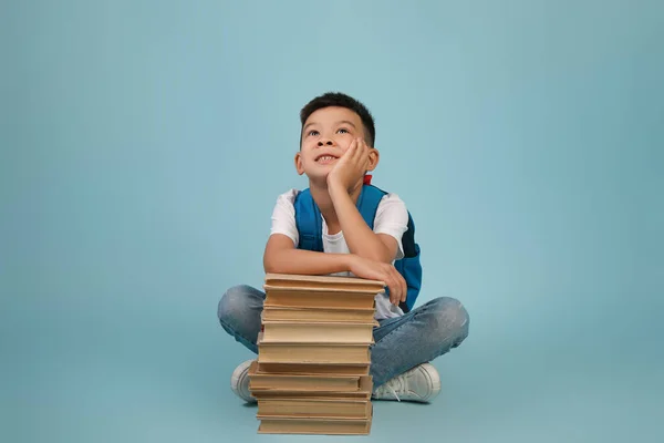 Dreamy poco coreano colegial apoyándose en pila de libros y mirando hacia arriba — Foto de Stock