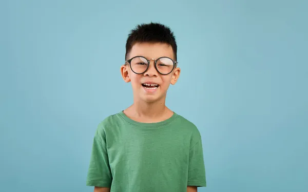 Porträt eines fröhlichen kleinen asiatischen Jungen mit Brille, der vor blauem Hintergrund posiert — Stockfoto