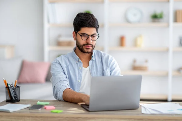 Απομακρυσμένη δουλειά. Συμπυκνωμένο Άραβας ελεύθερος επαγγελματίας τύπος που εργάζεται σε φορητό υπολογιστή στο γραφείο στο σπίτι, κάθεται στο γραφείο με compute — Φωτογραφία Αρχείου