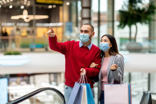 Millennial ποικιλόμορφο ζευγάρι φορώντας προστατευτικές μάσκες, ενώ ψώνια στο σούπερ μάρκετ, κρατώντας τσάντες shopper, αντίγραφο χώρο — Φωτογραφία Αρχείου