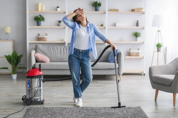 Втомлена жінка прибирає підлогу з пилососом у вітальні — стокове фото