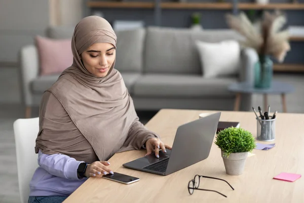 Dame musulmane assise à la table en utilisant la cellule et PC — Photo