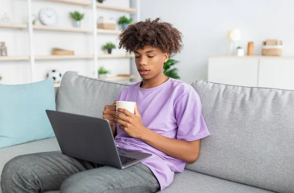 Webbbaserad utbildning. Svart tonåring pojke dricka kaffe, med videosamtal med andra studenter på laptop hemifrån — Stockfoto