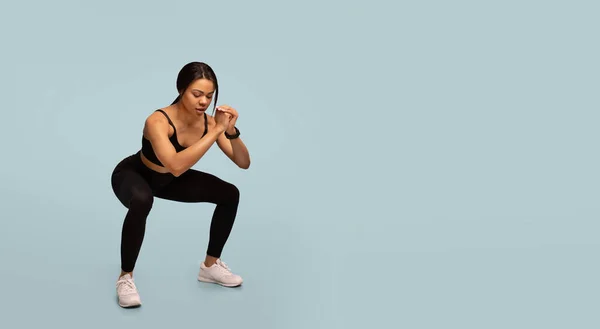 Edzés koncepció. Sportos afro-amerikai hölgy csinál mély guggolás testmozgás, edzés a kék háttér, panoráma — Stock Fotó