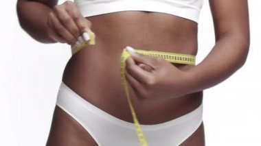Kilo kaybı ve zayıflama konsepti. Tanımlanamayan Afrikalı Amerikalı kadın model, belini bantla ölçüyor.