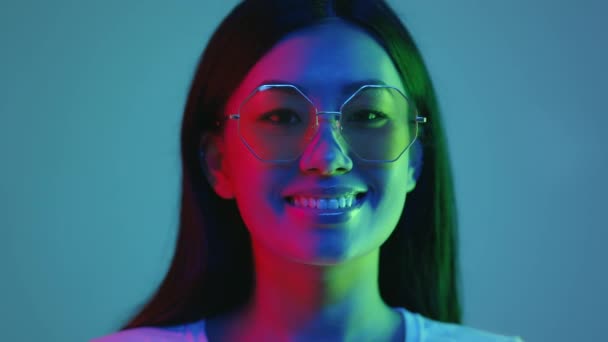 Стиль и концепция моды. Молодая позитивная азиатка в солнечных очках улыбается в камеру, позируя в ярких неоновых огнях — стоковое видео