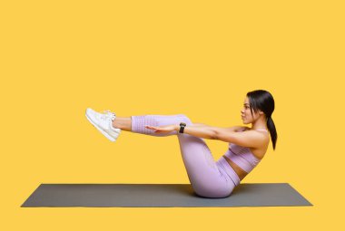 Spor yaparken karın kası egzersizi yapan Afro-Amerikan kadın sarı arka planda minderin üzerinde oturuyor.