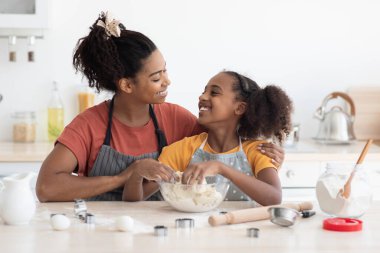 Şirin gülümseyen Afro-Amerikan anne ve kızı yemek pişirirken sarılıyorlar.