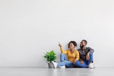 Rüyamda gülümseyen Afrikalı Amerikalı bir çift yerde oturmuş, saksıda gri duvarda bitki yetiştiriyor.