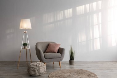 Koltuk, yastık, lamba, saksıda bitki, kanepe ve yerde yuvarlak halı, oturma odasının arka planında gri duvar.