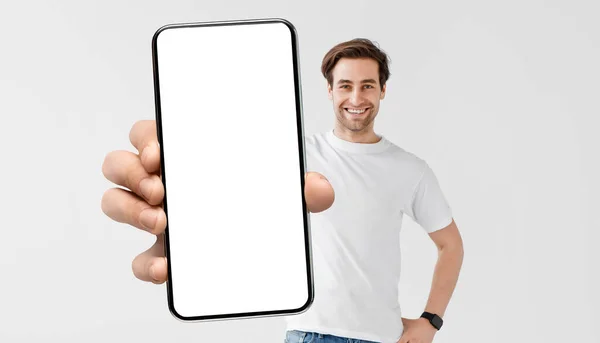 Imagen burlona de un joven guapo sosteniendo un teléfono inteligente con una gran pantalla en blanco — Foto de Stock