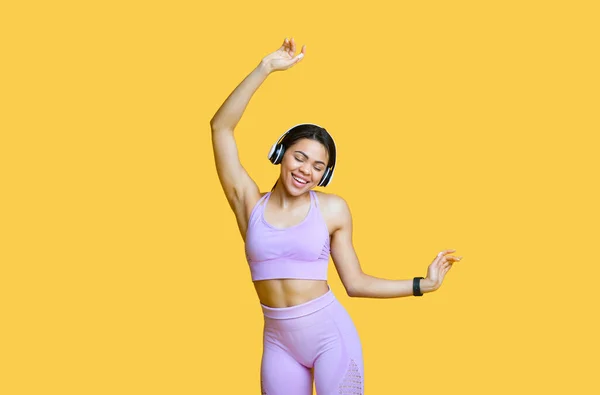 Deportiva mujer afroamericana en auriculares inalámbricos escuchando música y bailando, disfrutando de la lista de reproducción, fondo amarillo — Foto de Stock