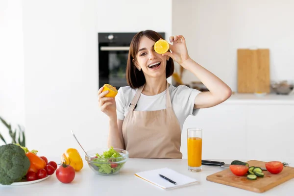 Lekfull ung kvinna som har roligt och täcker sina ögon med citronskivor, lurar runt i köket interiör — Stockfoto