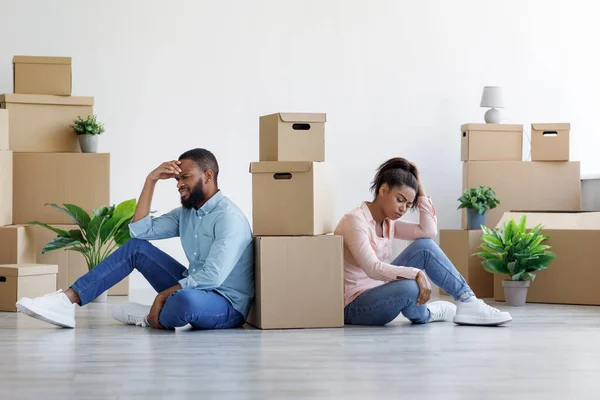 Cansado chateado jovem marido e mulher negra entre caixas de papelão com coisas e plantas em quarto vazio — Fotografia de Stock
