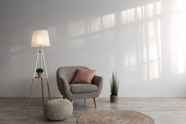 Sillón con almohada, lámpara, planta en maceta, otomana y alfombra redonda en el suelo sobre fondo de pared gris en la sala de estar —  Fotos de Stock