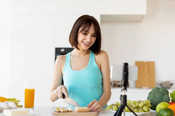 Happy fit kvinna förbereda fruktsallad, skära banan och spela in ny video för hennes mat blogg, stående i köket — Stockfoto