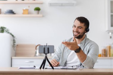 Sakallı, kulaklıklı, internetten sohbet eden ve jestler yapan olgun, beyaz bir öğrenci.