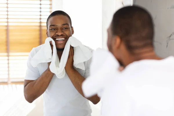 アフターシェービングケアコンセプト。バスルームでタオルで顔を拭くハンサムな黒男 — ストック写真